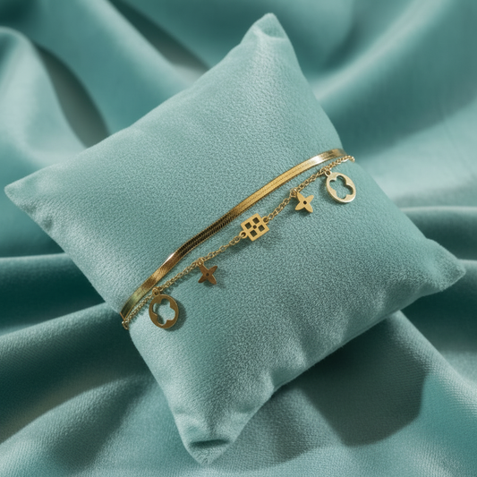 Gold double-layered herringbone and charm bracelet on slanted square teal cushion